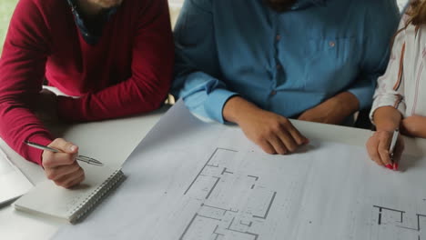 Three-architects-sitting-at-table-with-blueprints.